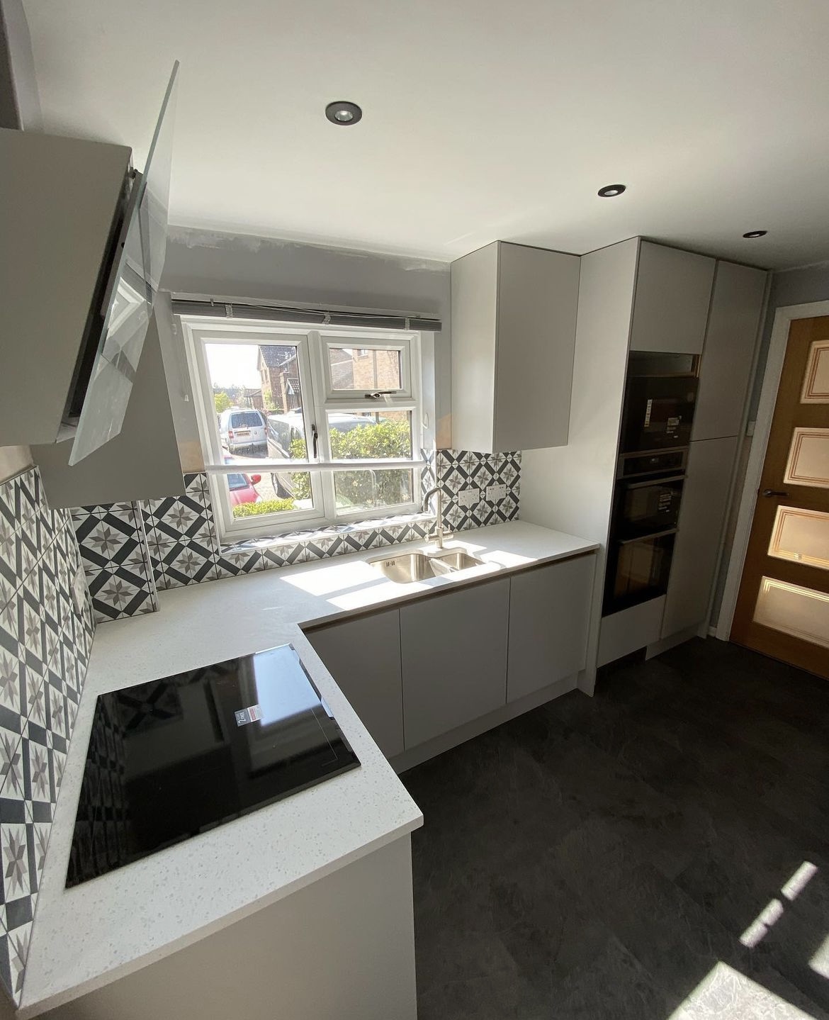 Light grey handleless kitchen with a patterned tile splashback and induction hob