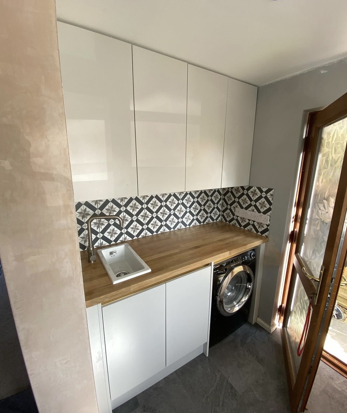 White utility room with an oak worktop, patterned tiles and a washing machine