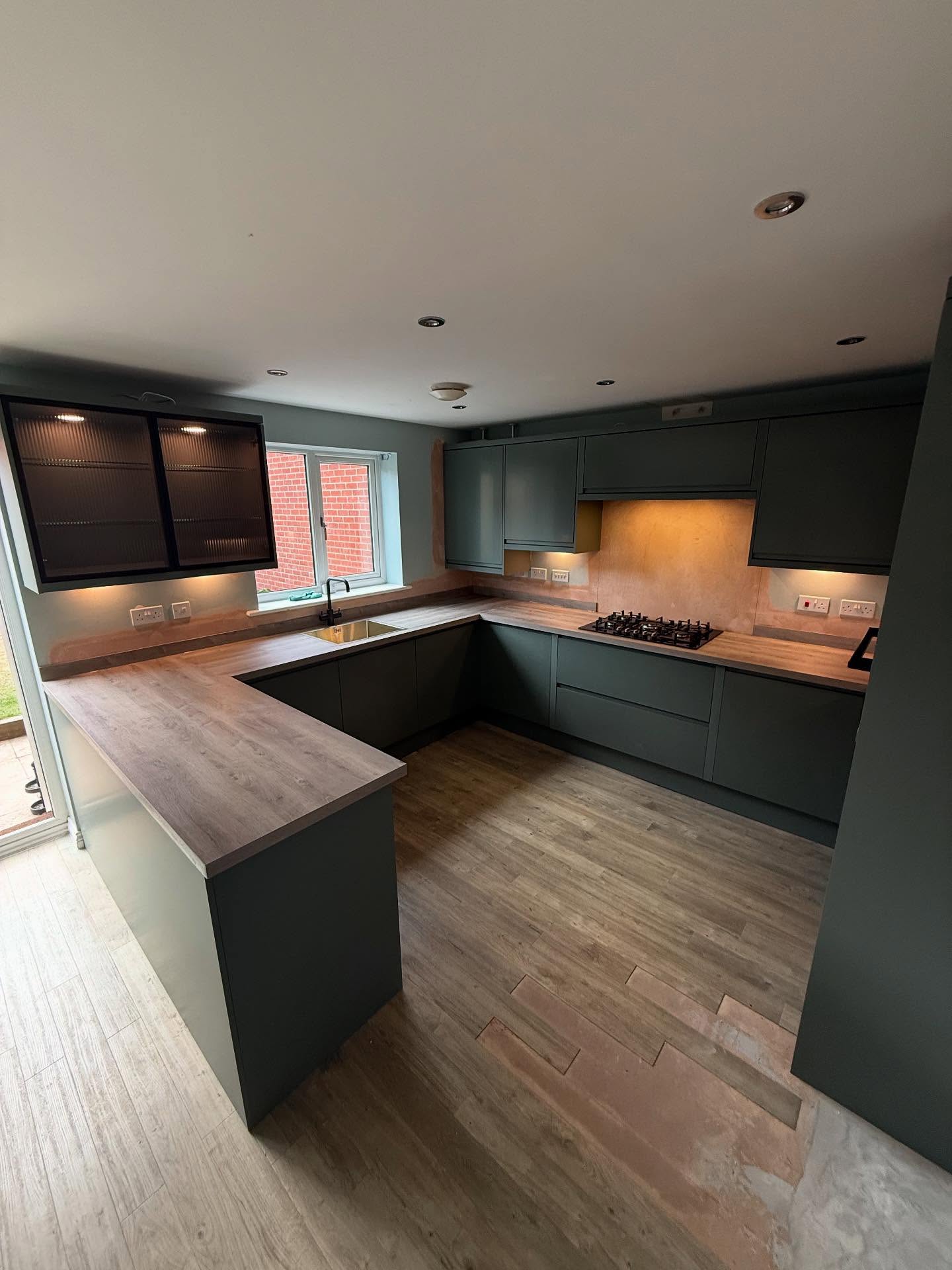 Dark green Magnet kitchen with wood worktops and lit wall units
